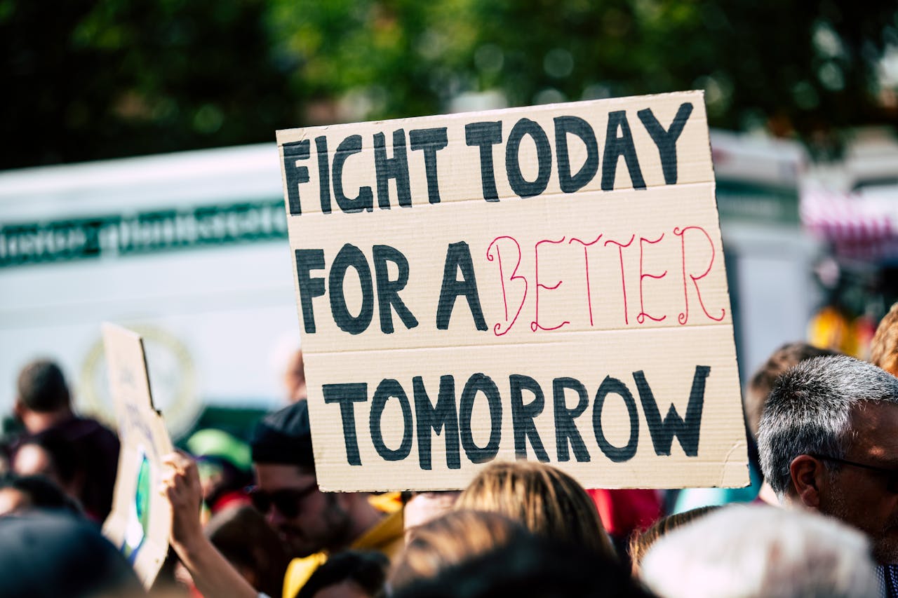 Crowd holding a protest sign with 'Fight Today for a Better Tomorrow', outdoors and during the day.